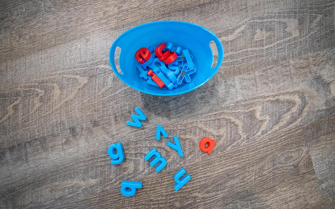 Colorful plastic letters scattered on the floor beside a blue bowl, representing early language learning and literacy development